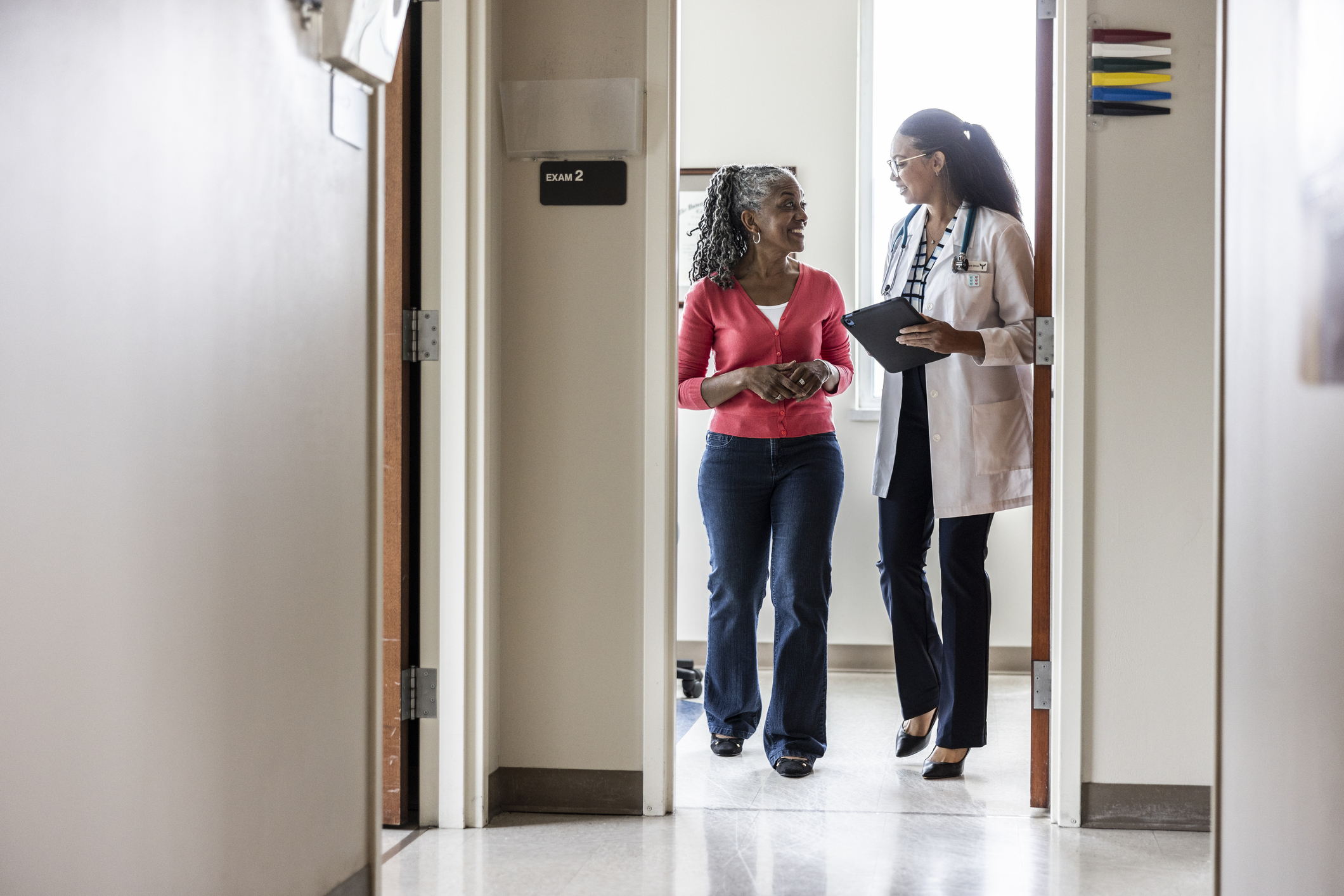 female doctor and older female patient walking through a doorway and talking