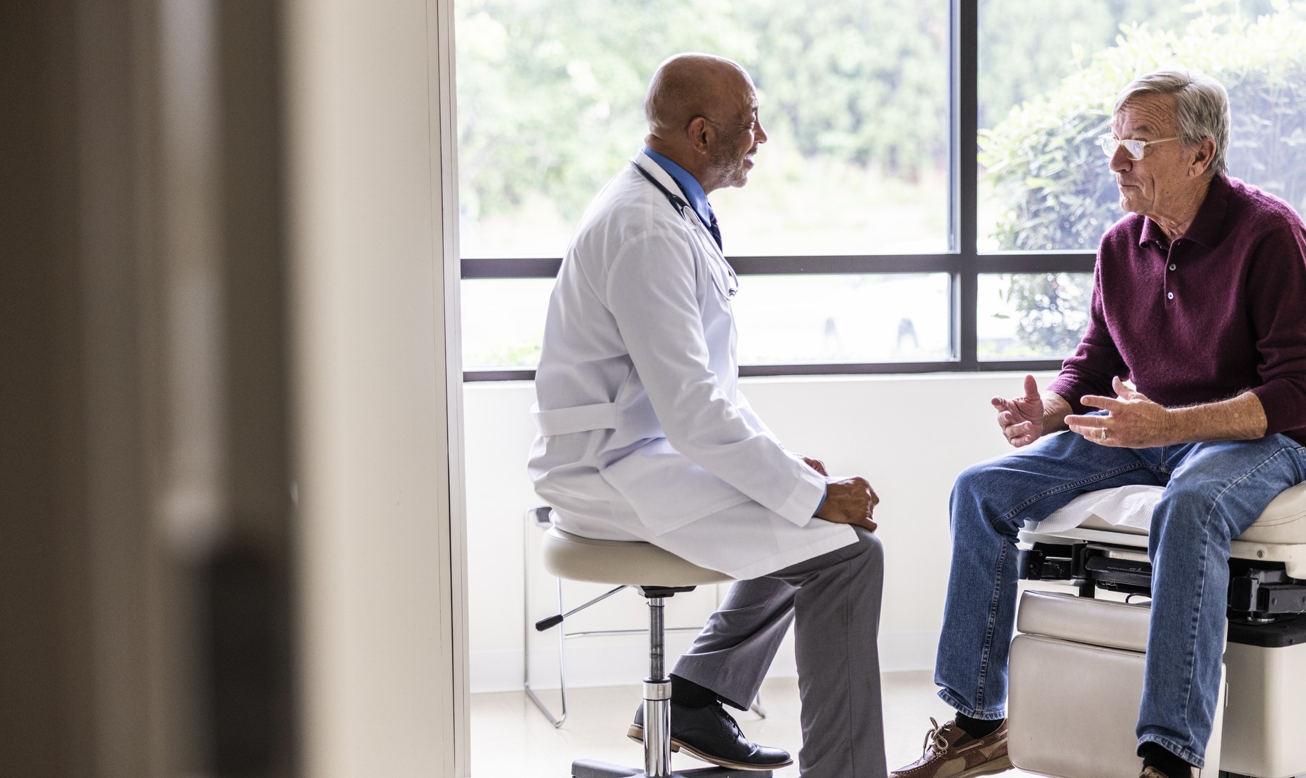 Male doctor talks to senior male patient in an exam room