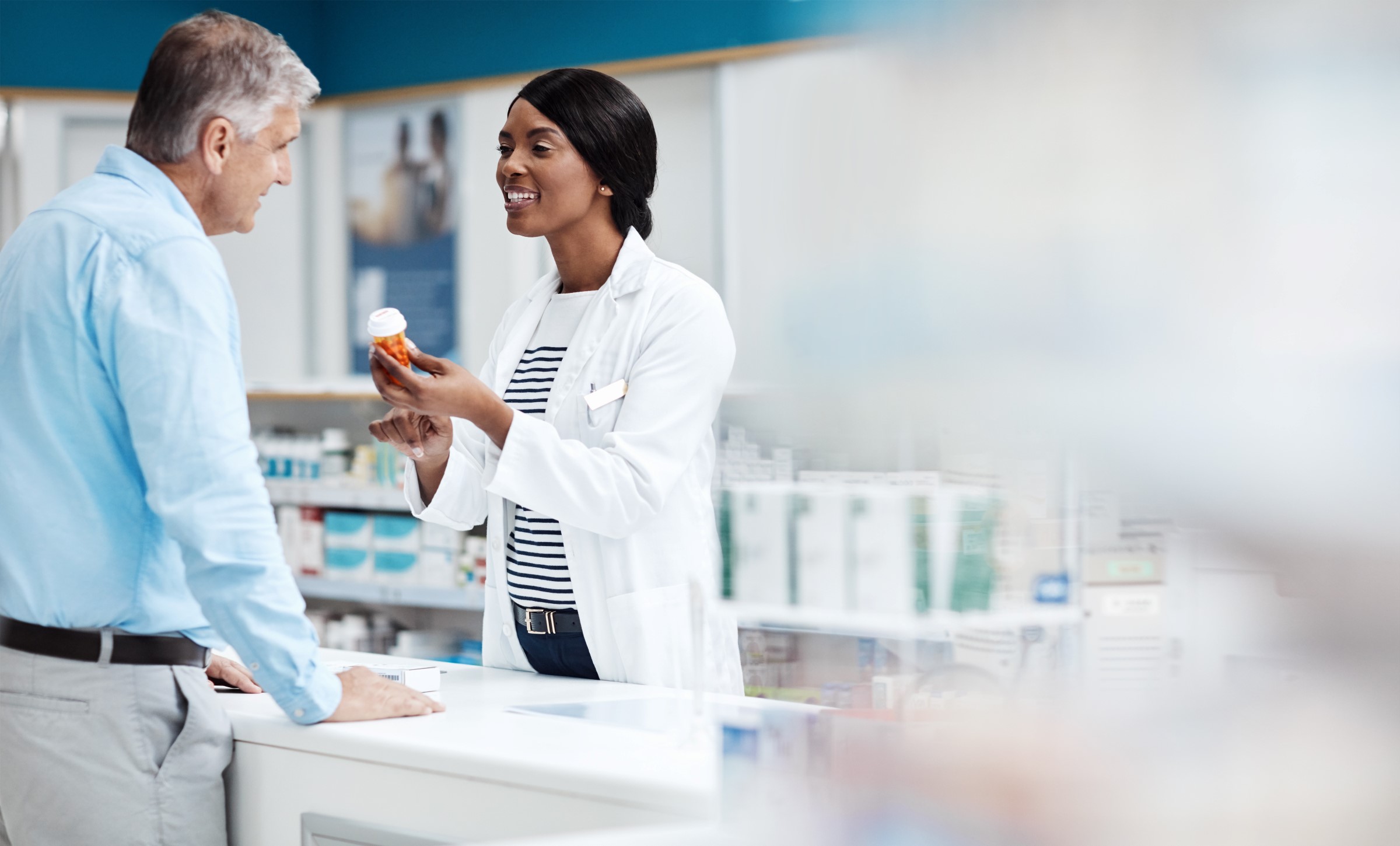Man speaking with a female pharmacist showing him a prescription bottle