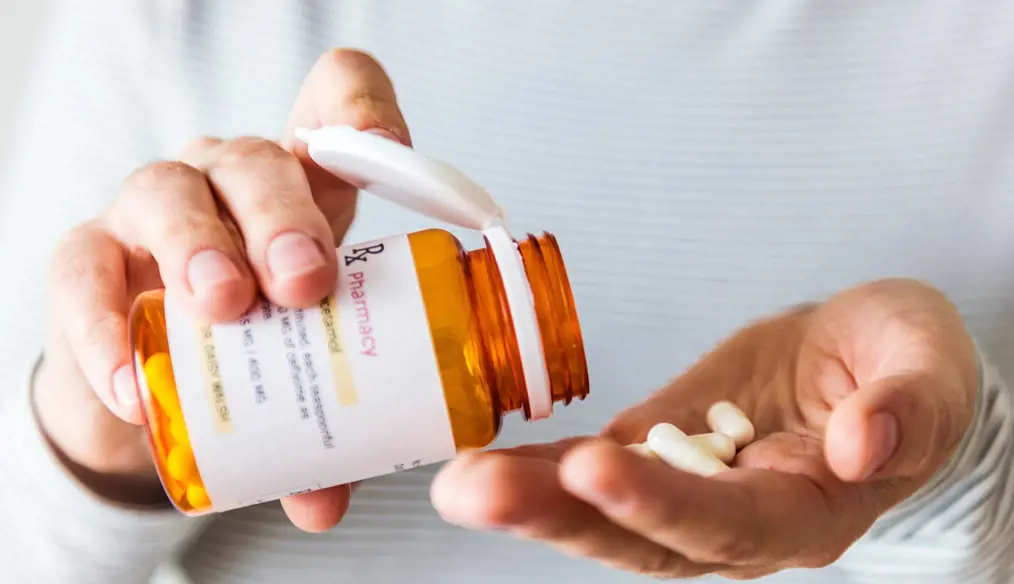 closeup of one hand holding a pill bottle dispensing pills into the other hand
