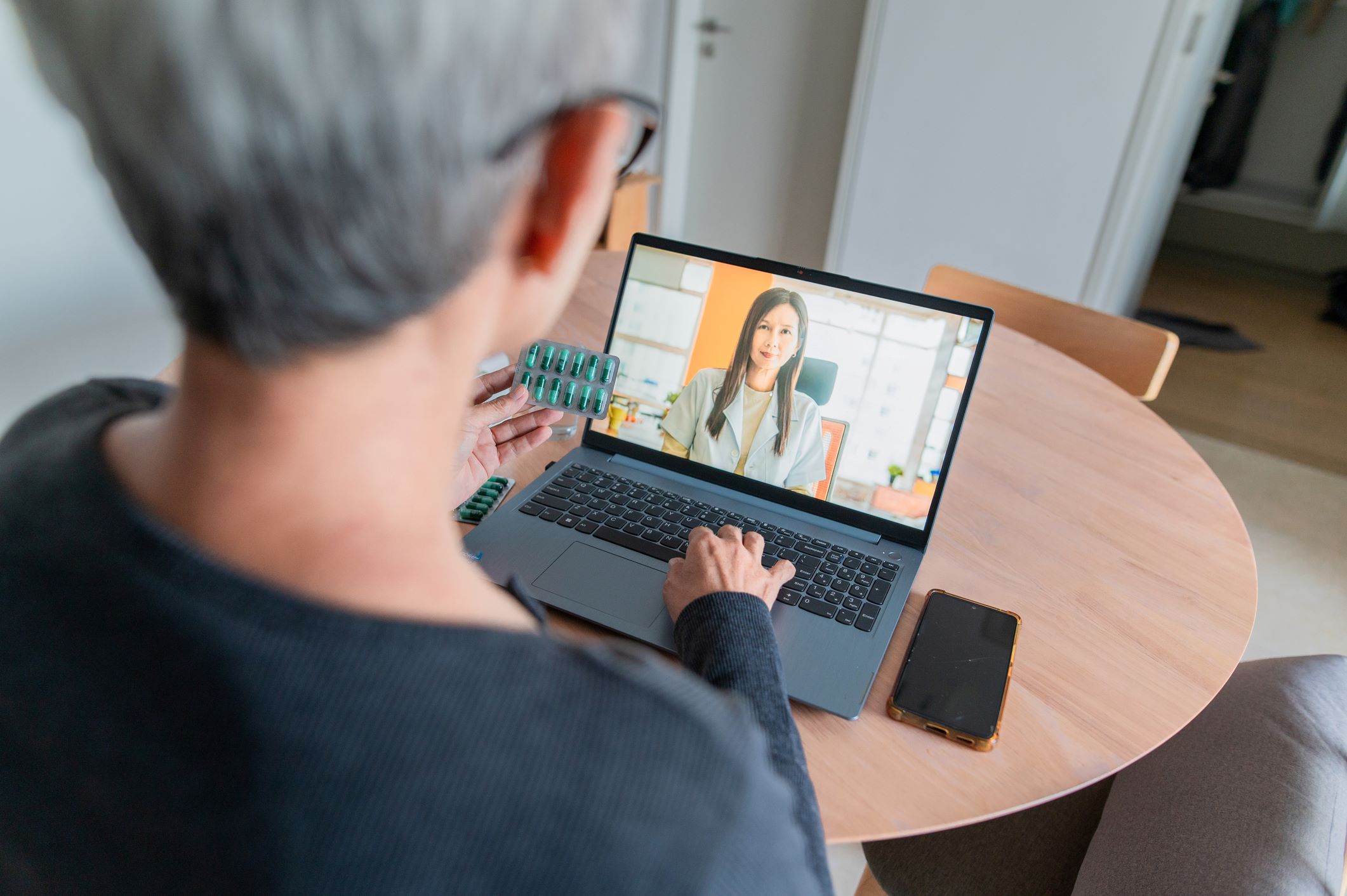view of woman from behind holding medication and talking to her doctor on computer