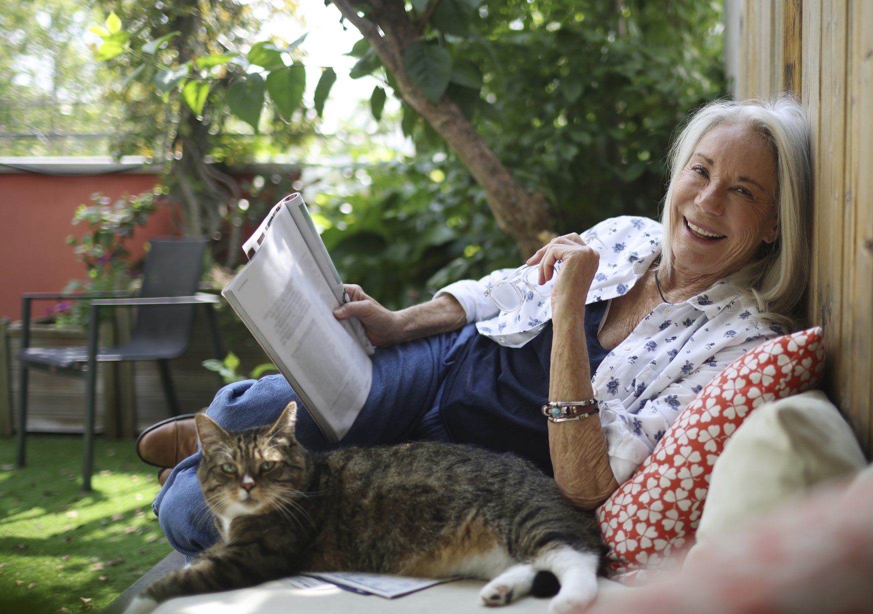 Senior woman laughing and relaxing with a magazine in her backyard