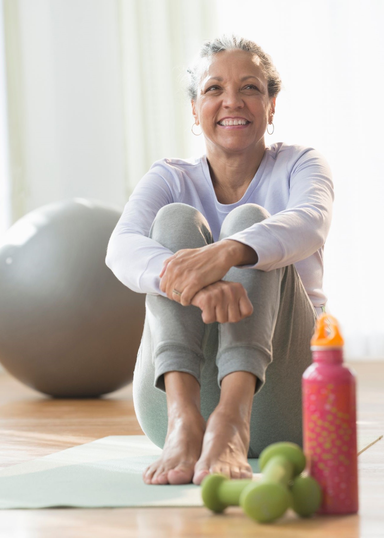 older woman with water bottle and weights sitting and relaxing after a workout
