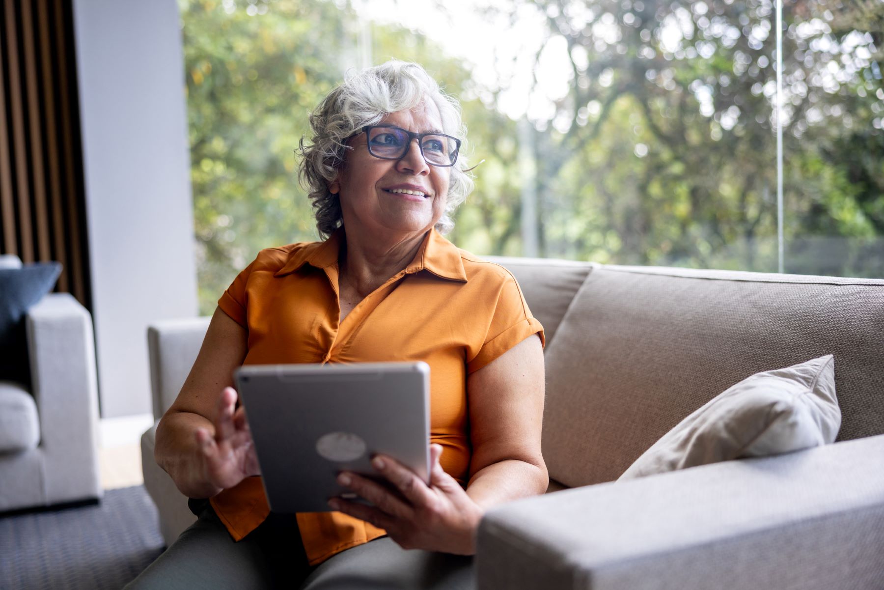 thoughtful senior woman using a digital tablet smiling into the distance
