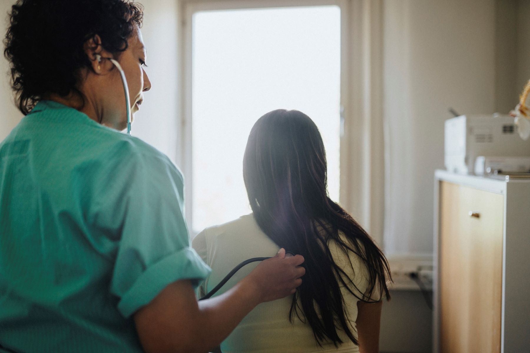 rear view of doctor holding stethescope on female patient's back